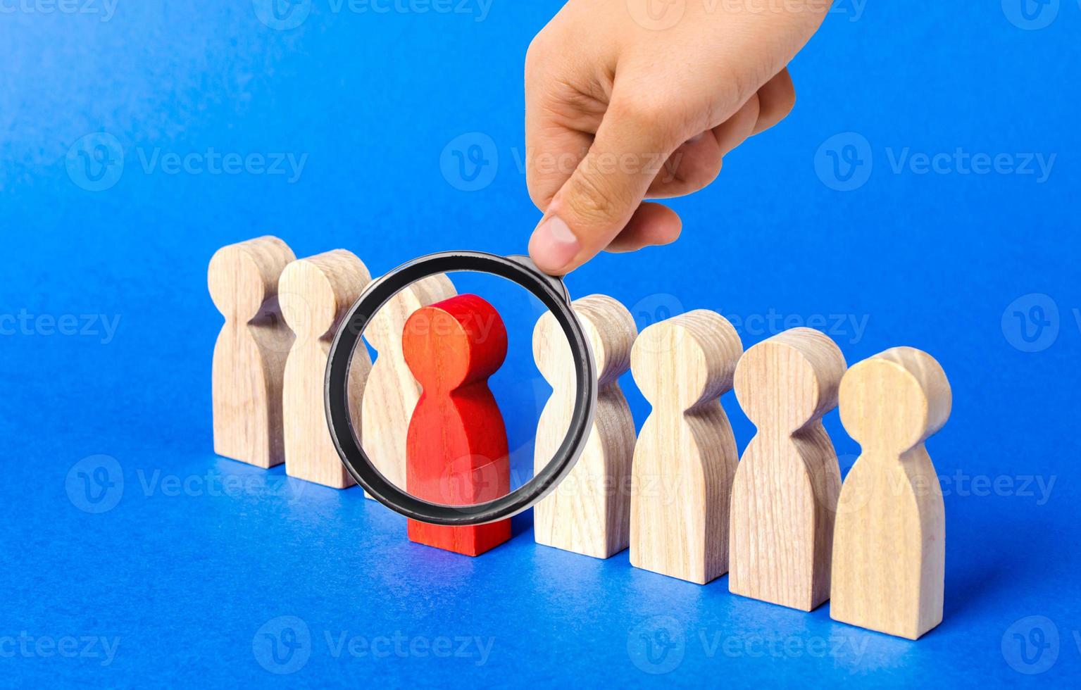 A magnifying glass looks at a red figure person comes out of people line. Leadership qualities, talented employee. HR is looking for new employees, choice among candidates. A suitable candidate photo