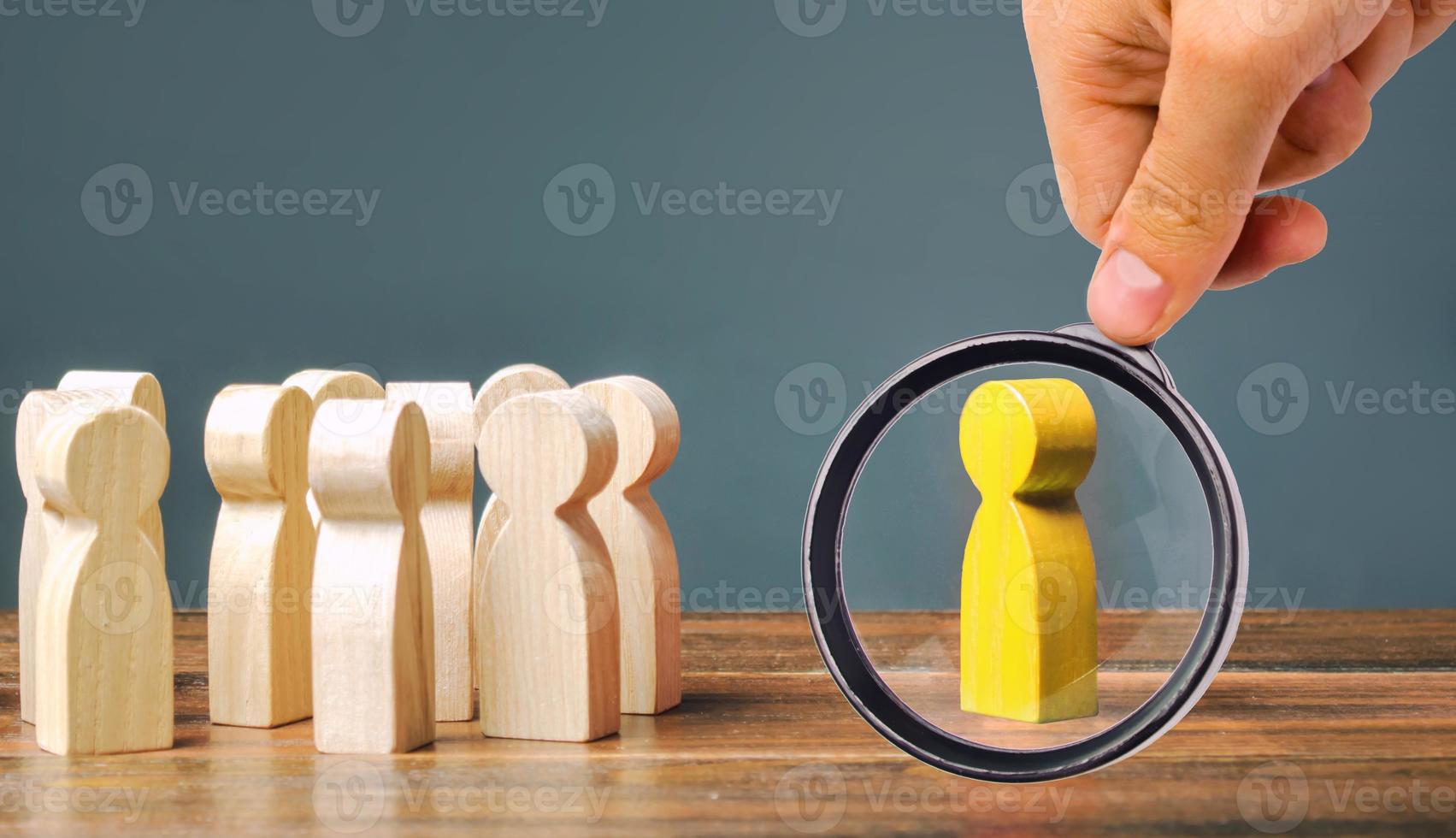 A magnifying glass looks at a yellow figurine of a man stands aside from the crowd of people. Asociality, sociopathy. Rejected from society, lonely. Development of leadership and social qualities. photo