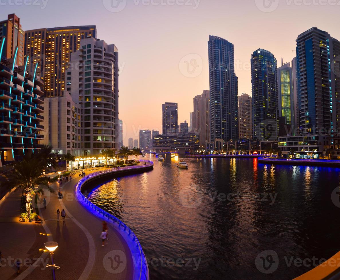 Dubai, UAE, 2022 - Dubai Marina skyline with illuminated sky scrappers,buildings and moving boats showing reflection on water captured from Marina Mall , Dubai, UAE. photo