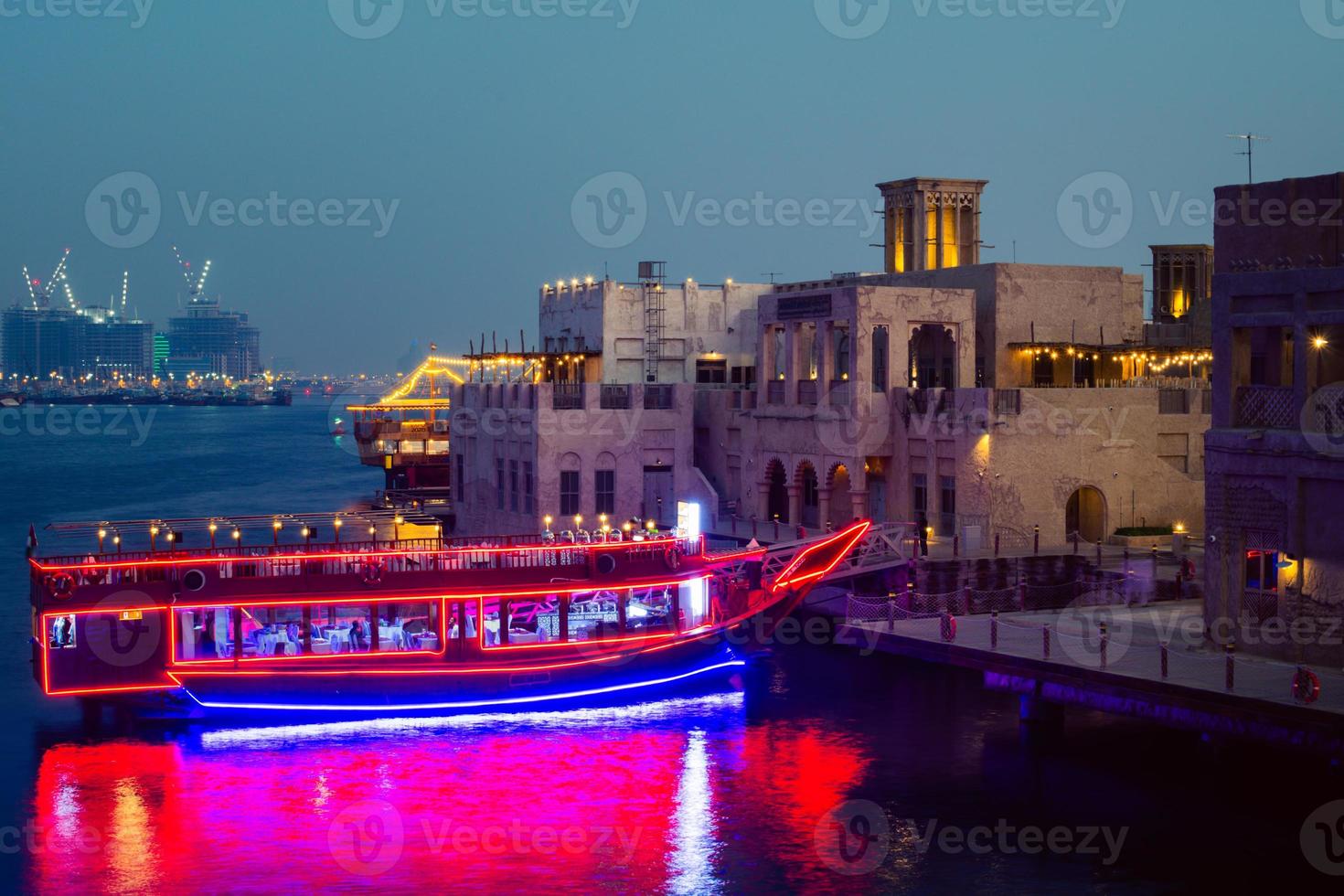 Dubai, UAE, 2022- illuminated vintage vessel restaurant - boat docked by beautiful old buildings in old Dubai creek district in summer photo