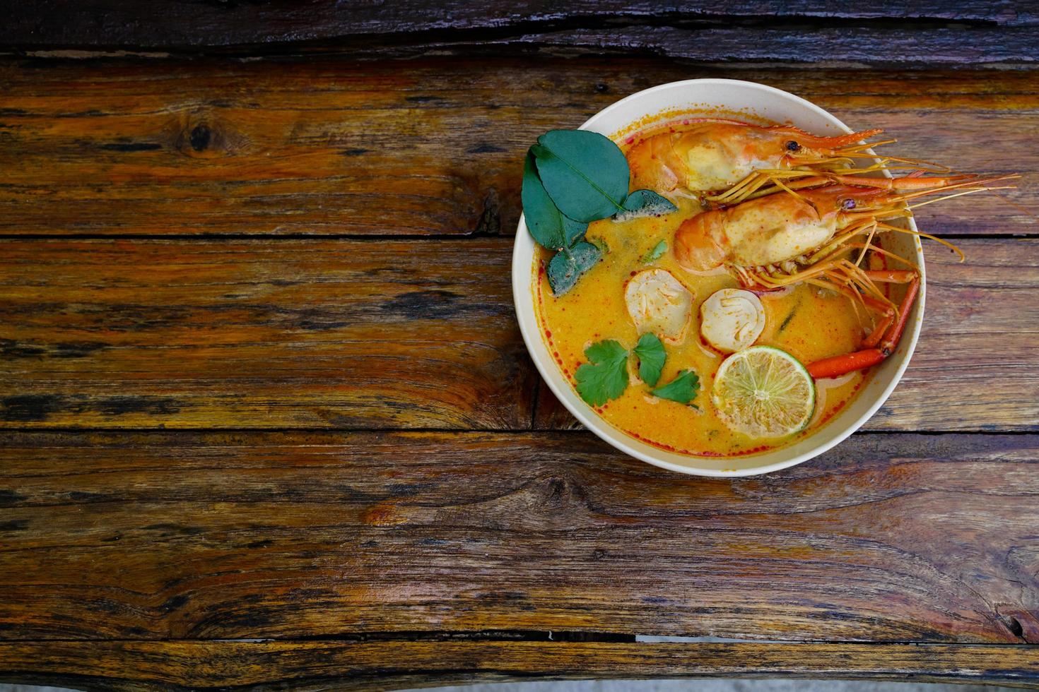 tom yum kung en una taza sobre un piso de madera, tom yum kung es también el plato nacional de tailandia. y es un alimento que es famoso en todo el mundo. foto