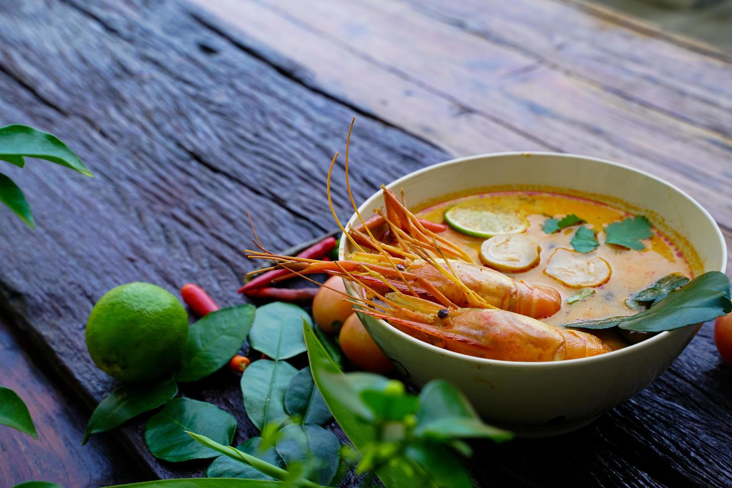 tom yum kung en una taza sobre un piso de madera, tom yum kung es también el plato nacional de tailandia. y es un alimento que es famoso en todo el mundo. foto