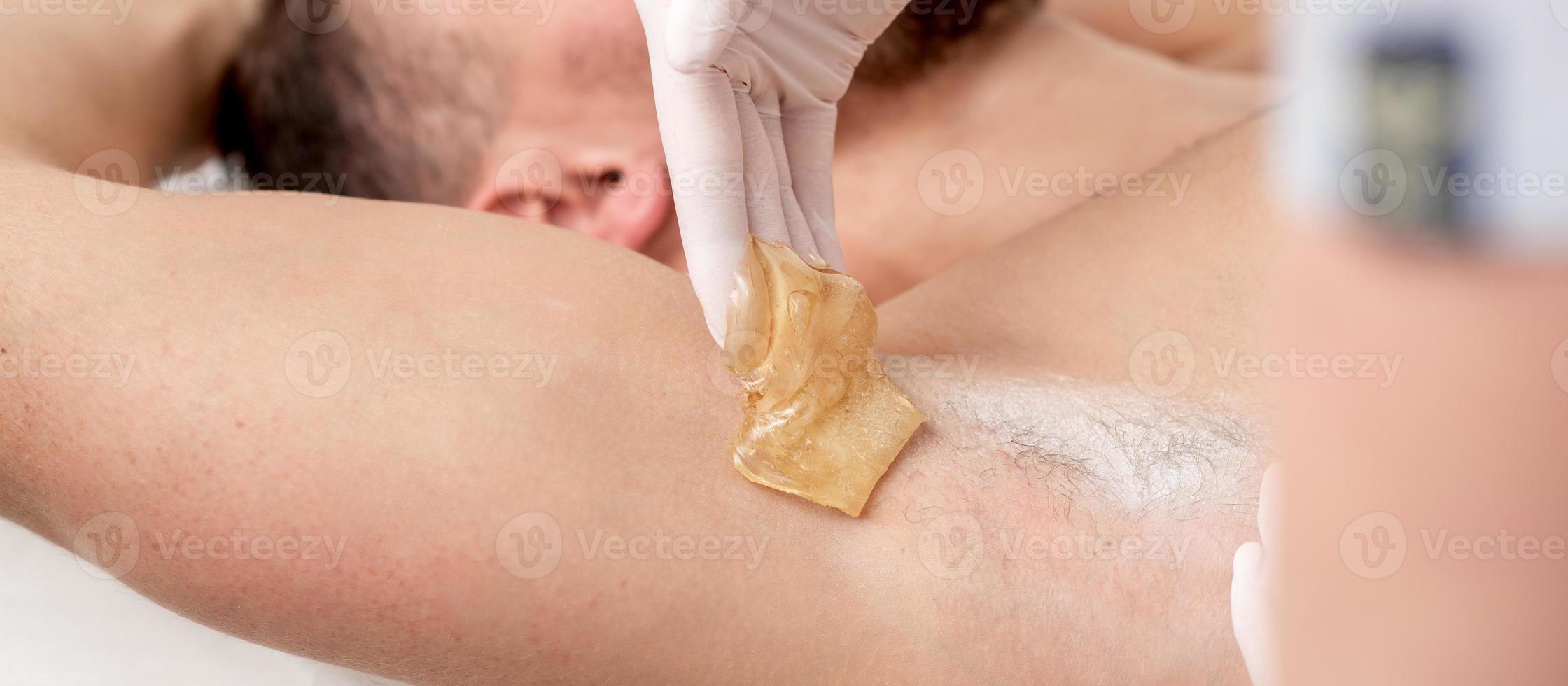 Cosmetologist applying wax paste on male armpit photo
