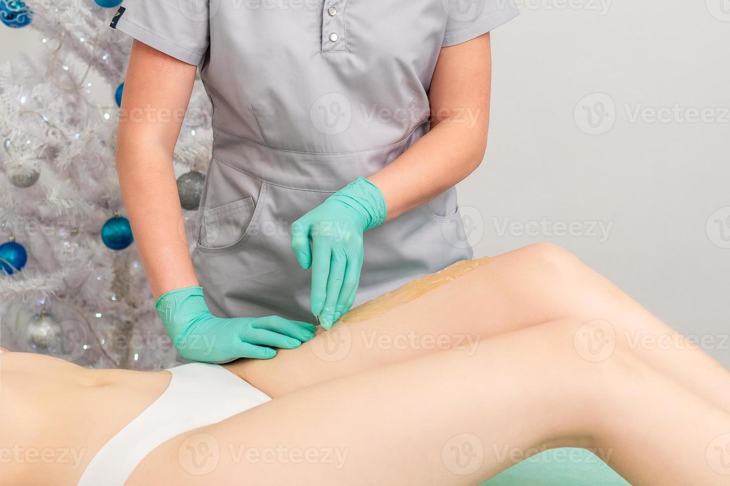 Cosmetologist in gloves applying paste for sugaring depilation photo