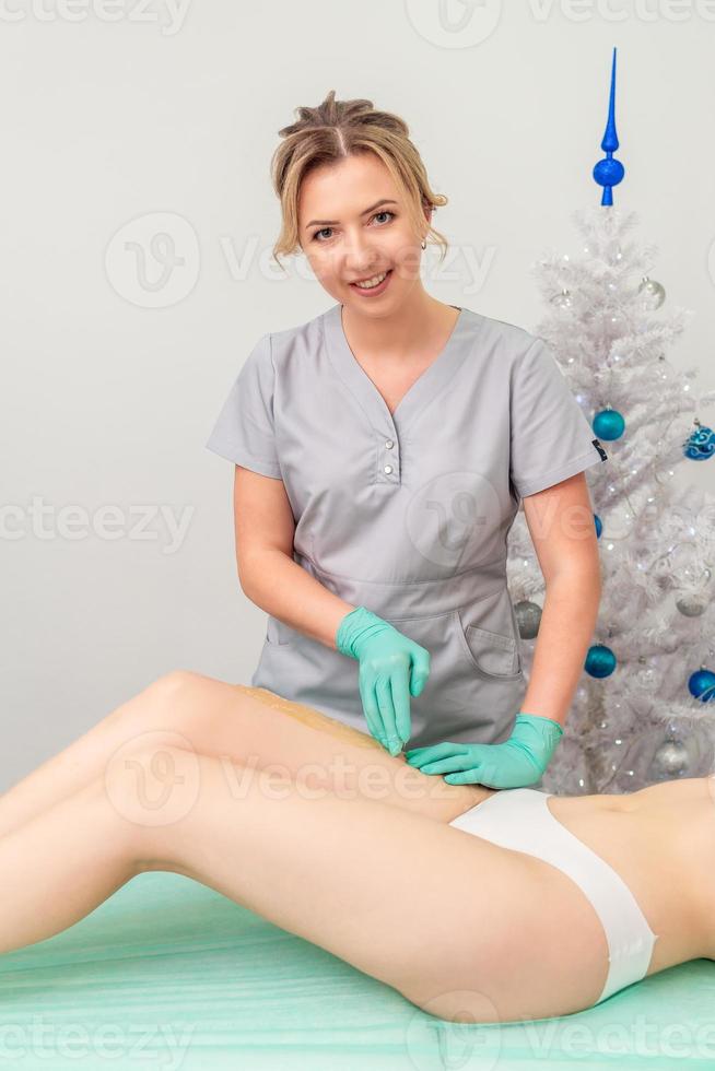 Cosmetologist in gloves applying paste for sugaring depilation photo