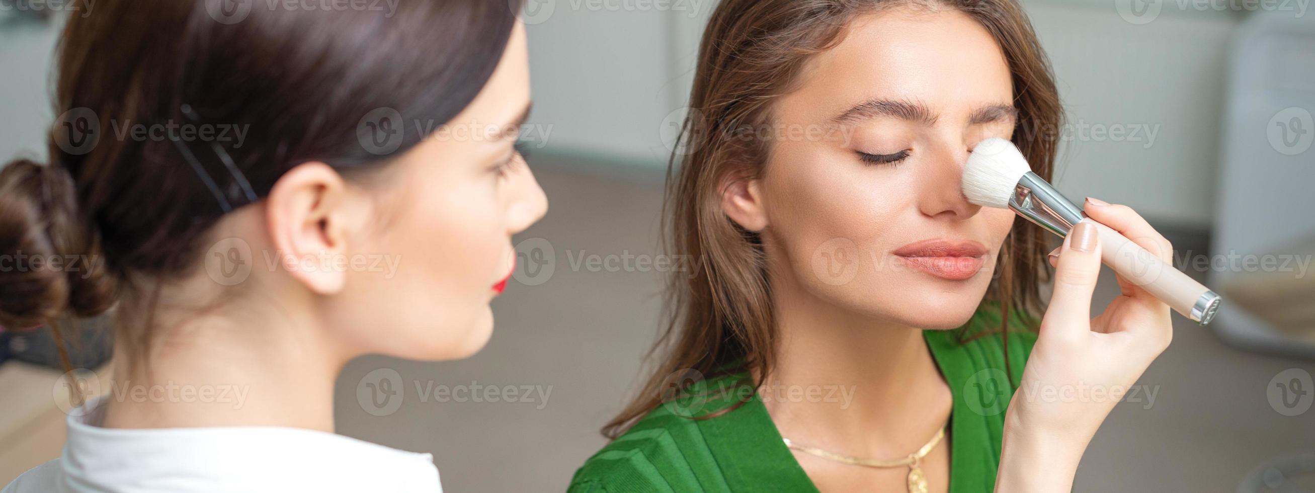 Makeup artist applying dry cosmetic tonal foundation on nose photo