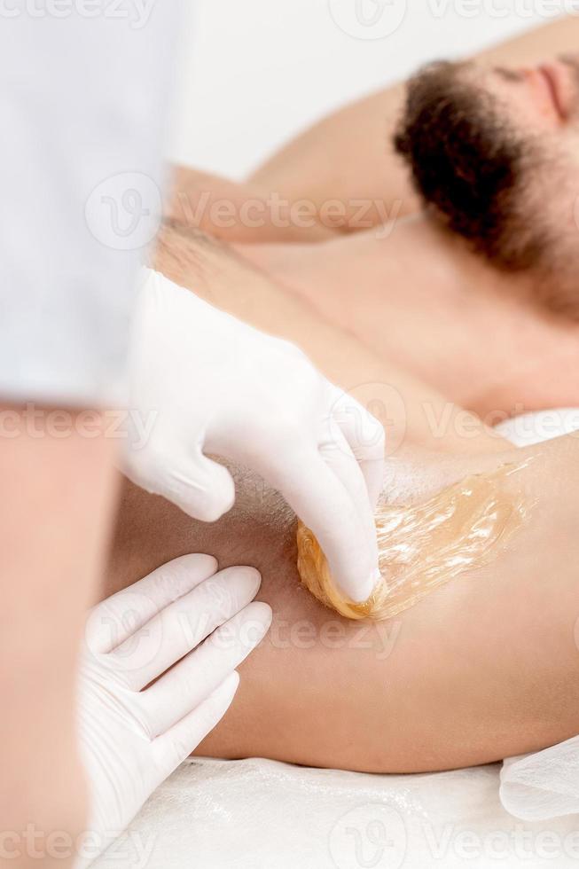 Cosmetologist applying wax paste on male armpit photo