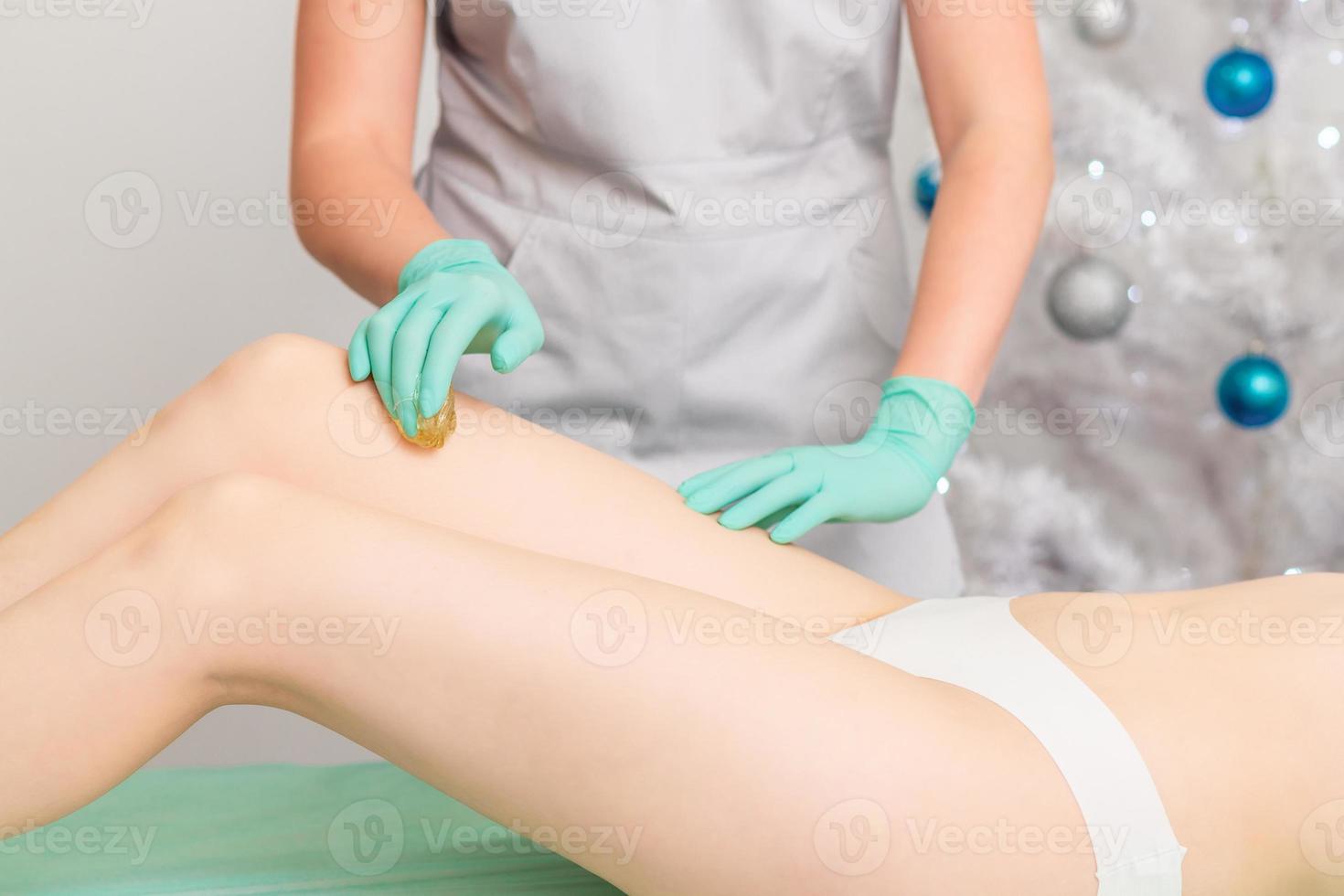 Beautician waxing female legs. photo