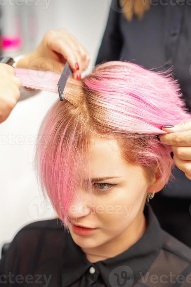 peluquero alisa el pelo rosa de mujer con plancha de pelo. foto