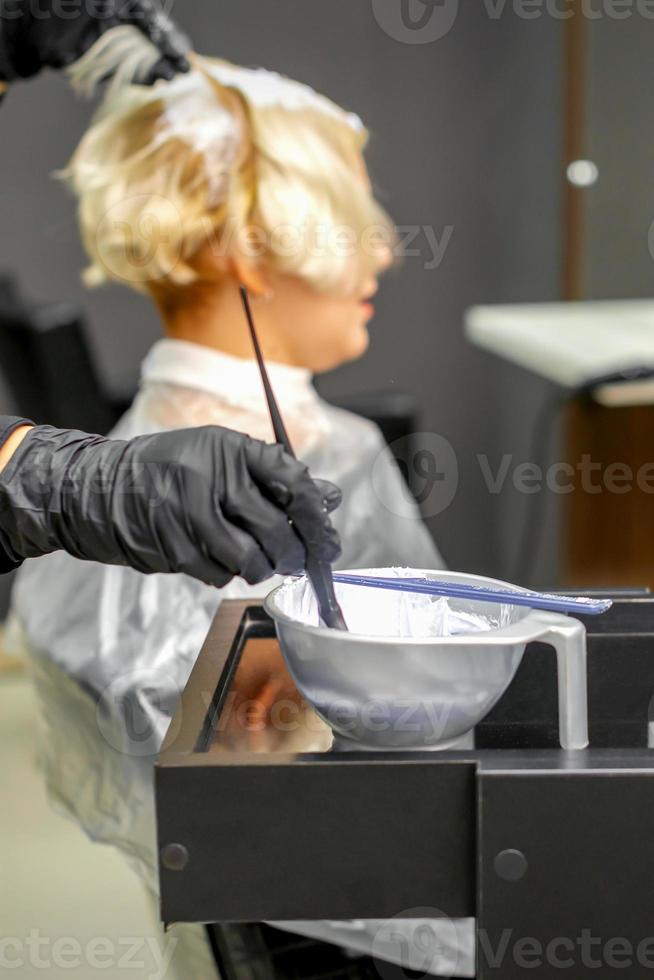Hairdresser dyeing hair of young woman photo