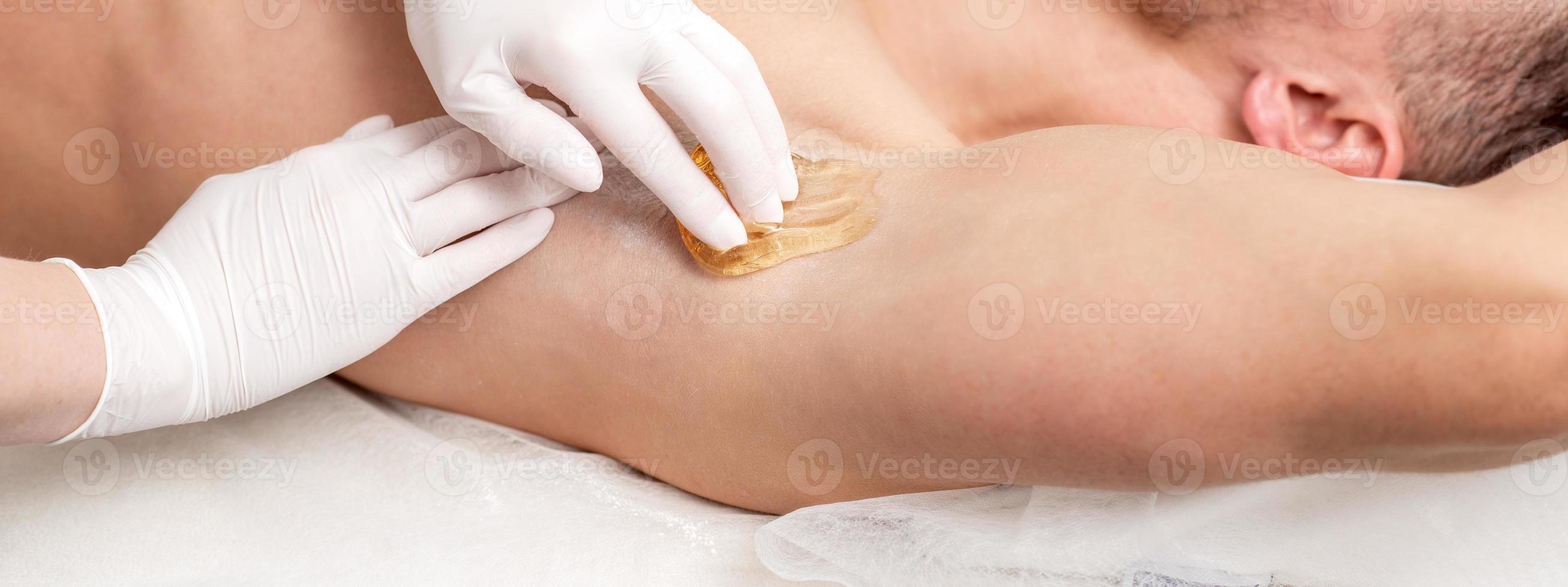 Cosmetologist applying wax paste on male armpit photo