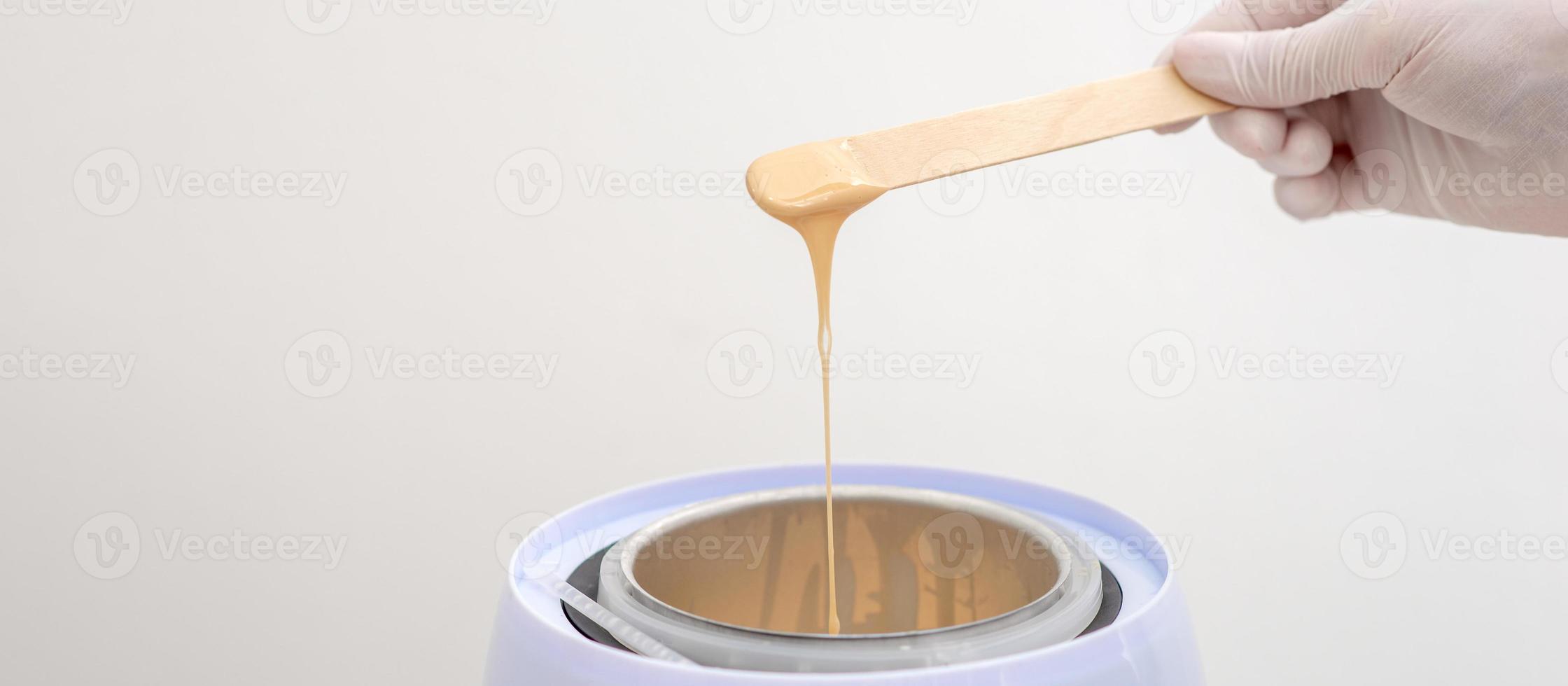 Wax heater with hot wax on wooden spatula photo