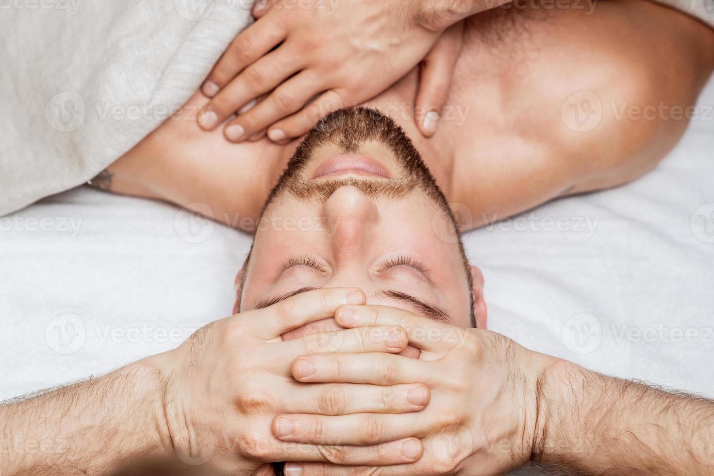 Man receiving head massage by two masseurs photo