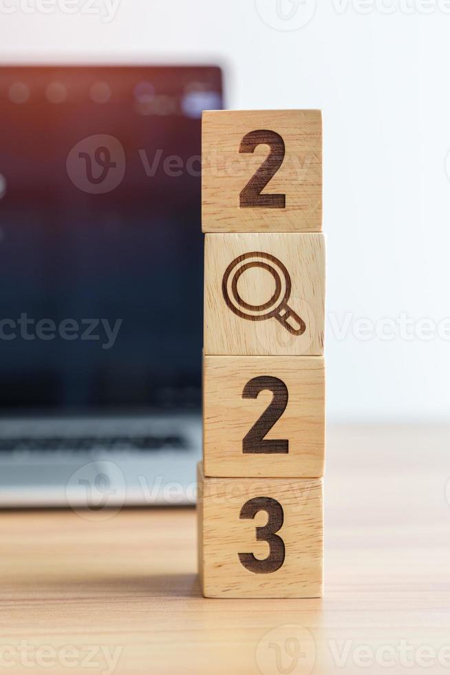 2023 block with magnifying glass icon against laptop background. Hiring, recruitment, job, jobless SEO, Search Engine Optimization and New Year concepts photo