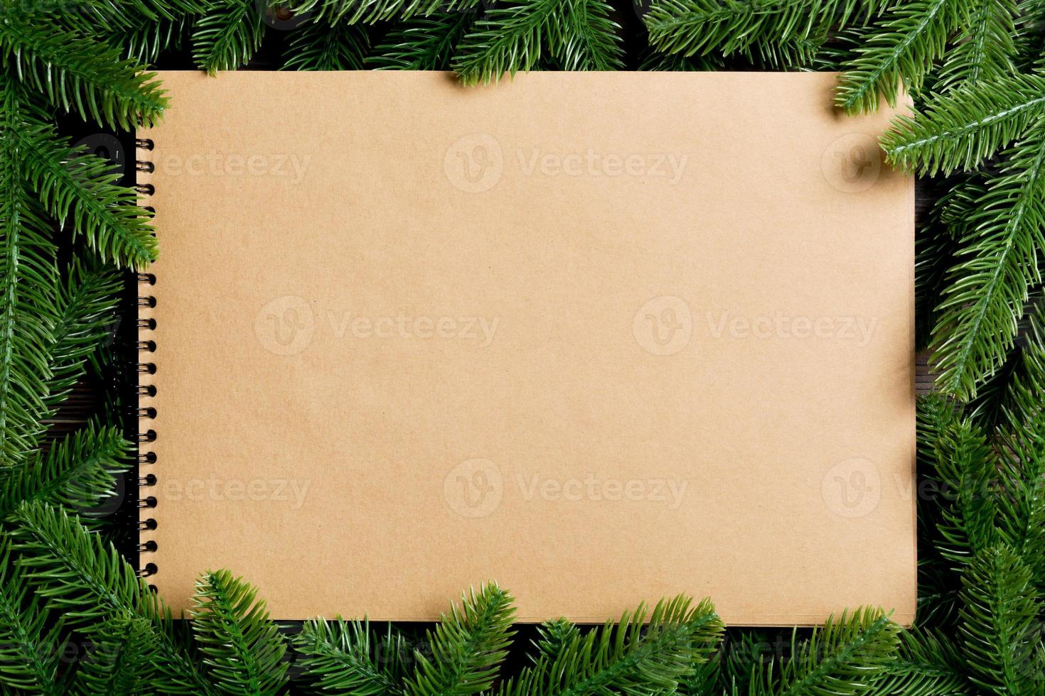 Top view of notebook made of craft paper decorated with a frame made of fir tree on wooden background. New Year time concept photo
