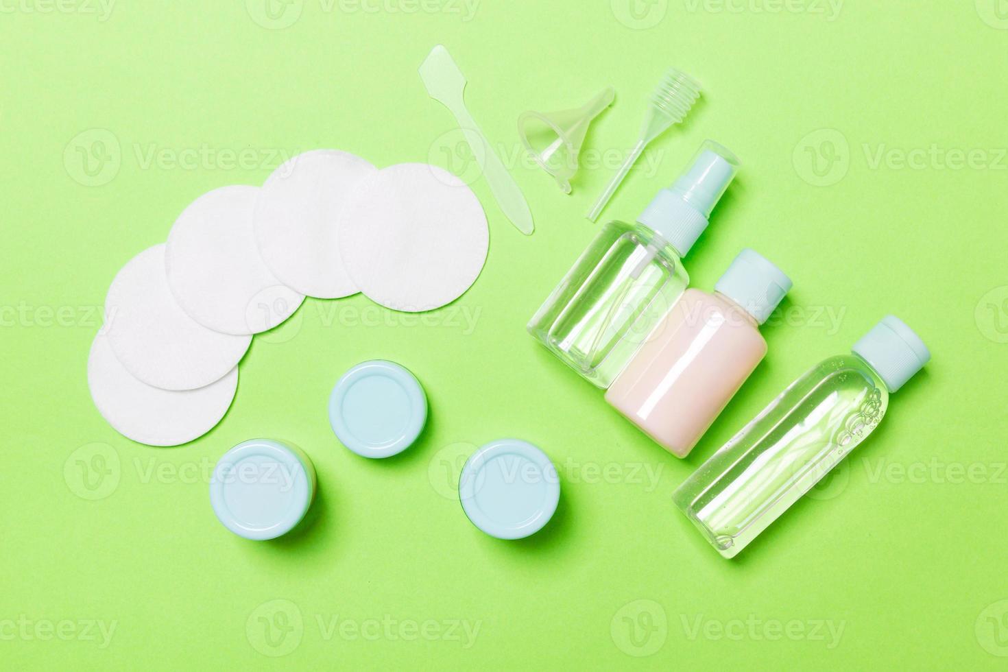 Top view of means for face care bottles and jars of tonic, micellar cleansing water, cream, cotton pads on green background. Bodycare concept with empty cpace for your ideas photo