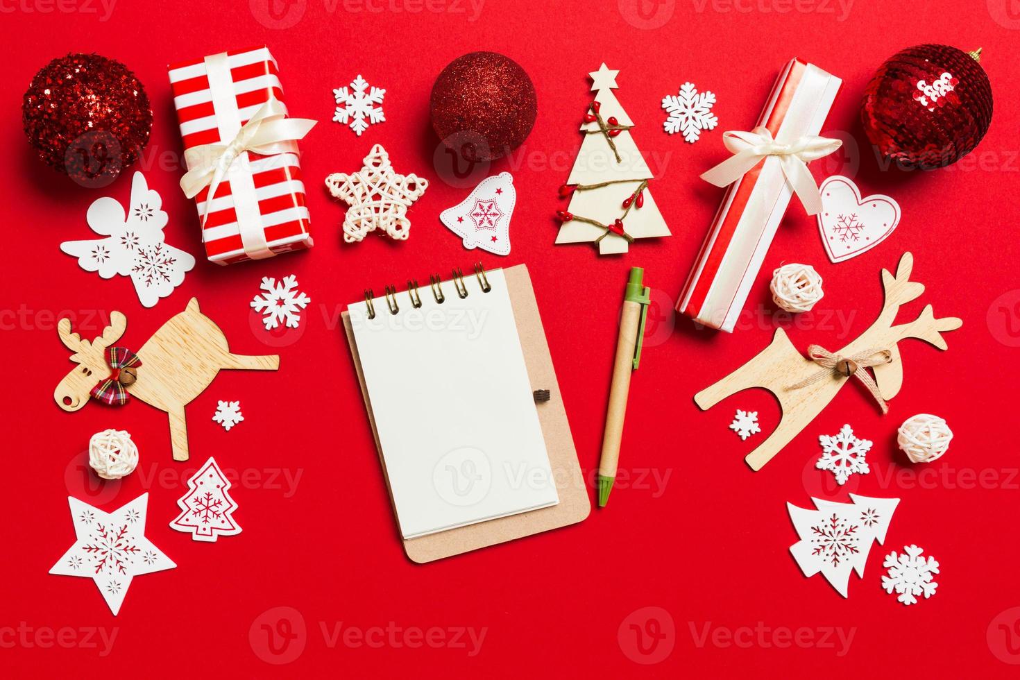 vista superior del cuaderno sobre fondo rojo hecho de adornos navideños. concepto de tiempo de año nuevo foto