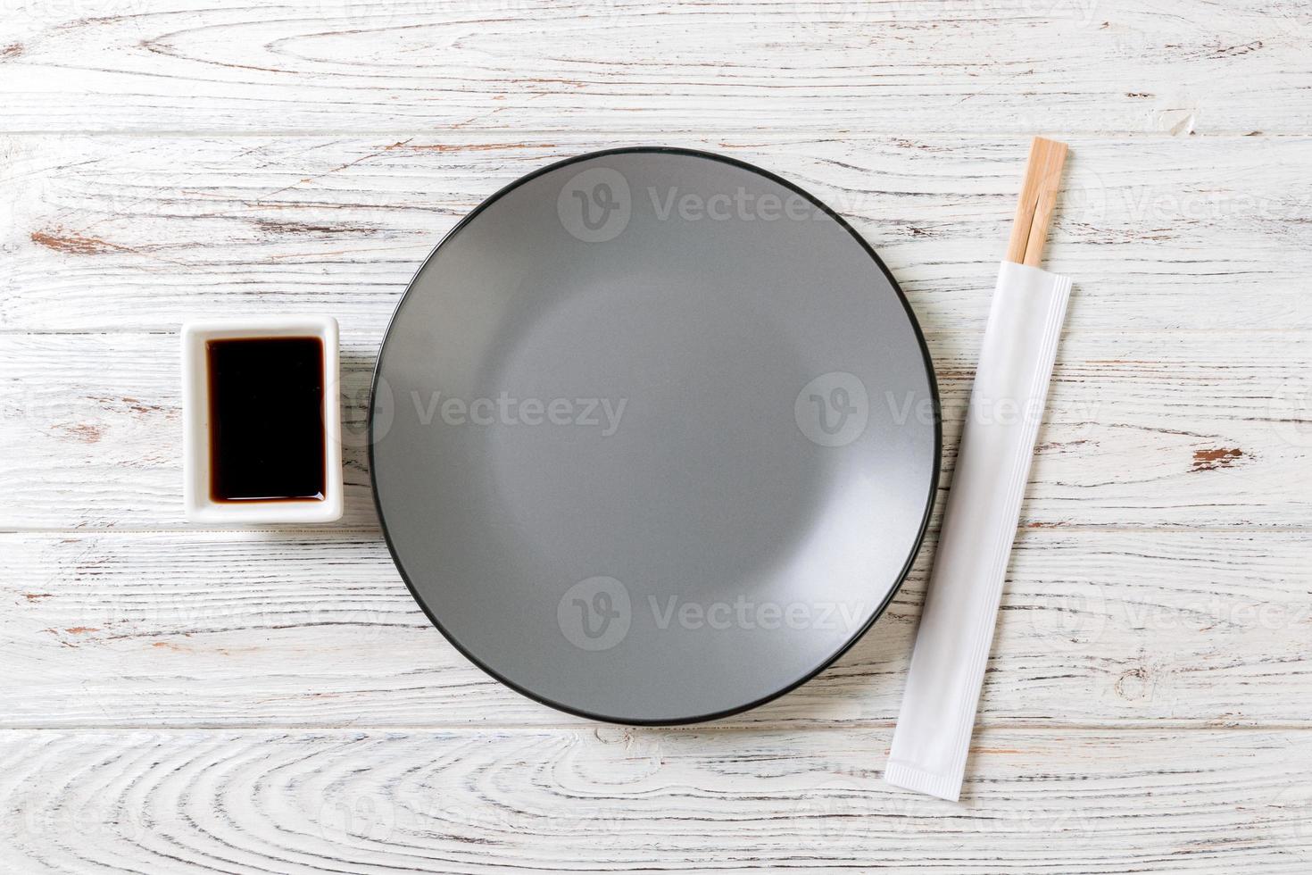 Empty grey round plate with chopsticks for sushi and soy sauce on wooden background. Top view with copy space photo