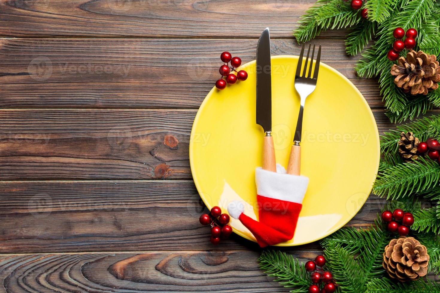 Top view of Christmas dinner on wooden background. Plate, utensil, fir tree and holiday decorations with copy space. New Year time concept photo