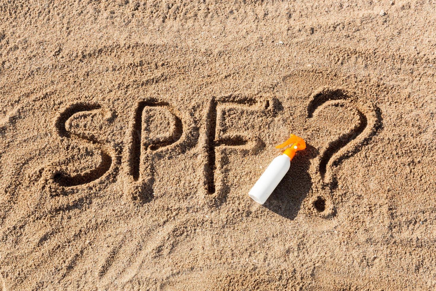 Sun protect factor. SPF word written on the sand and white bottle with suntan cream with question mark. Skin care concept background photo