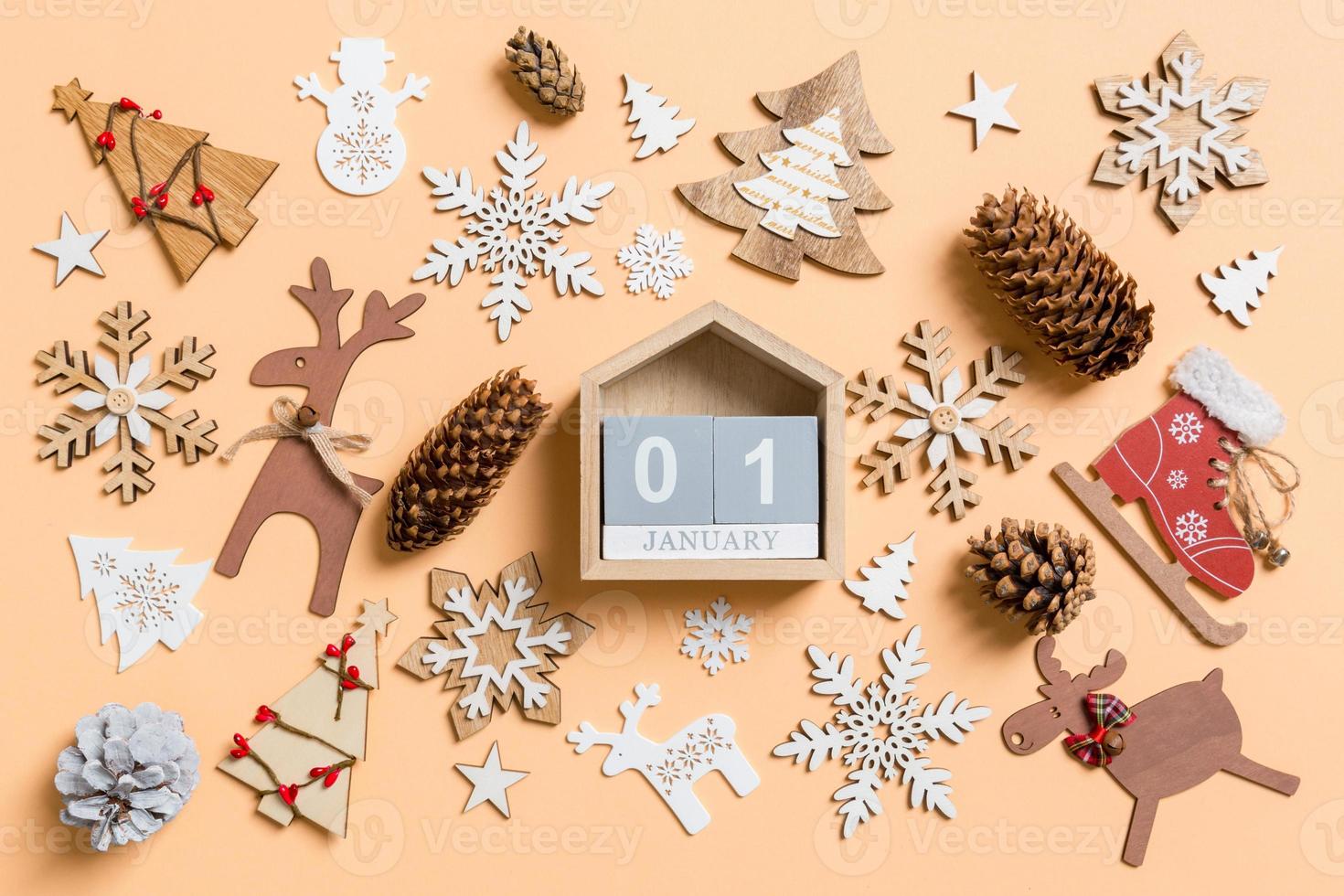 Top view of wooden calendar surrounded with New Year toys and decorations on orange background. The first of January. Christmas time concept photo