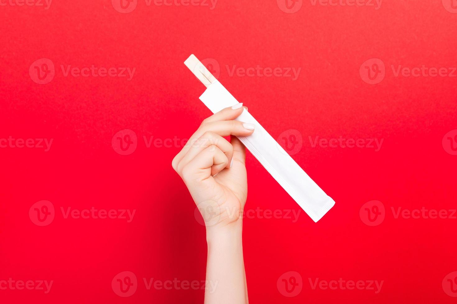 Woman's hand holding chopsticks in a pack on red background. Chinese food concept with empty space for your design photo
