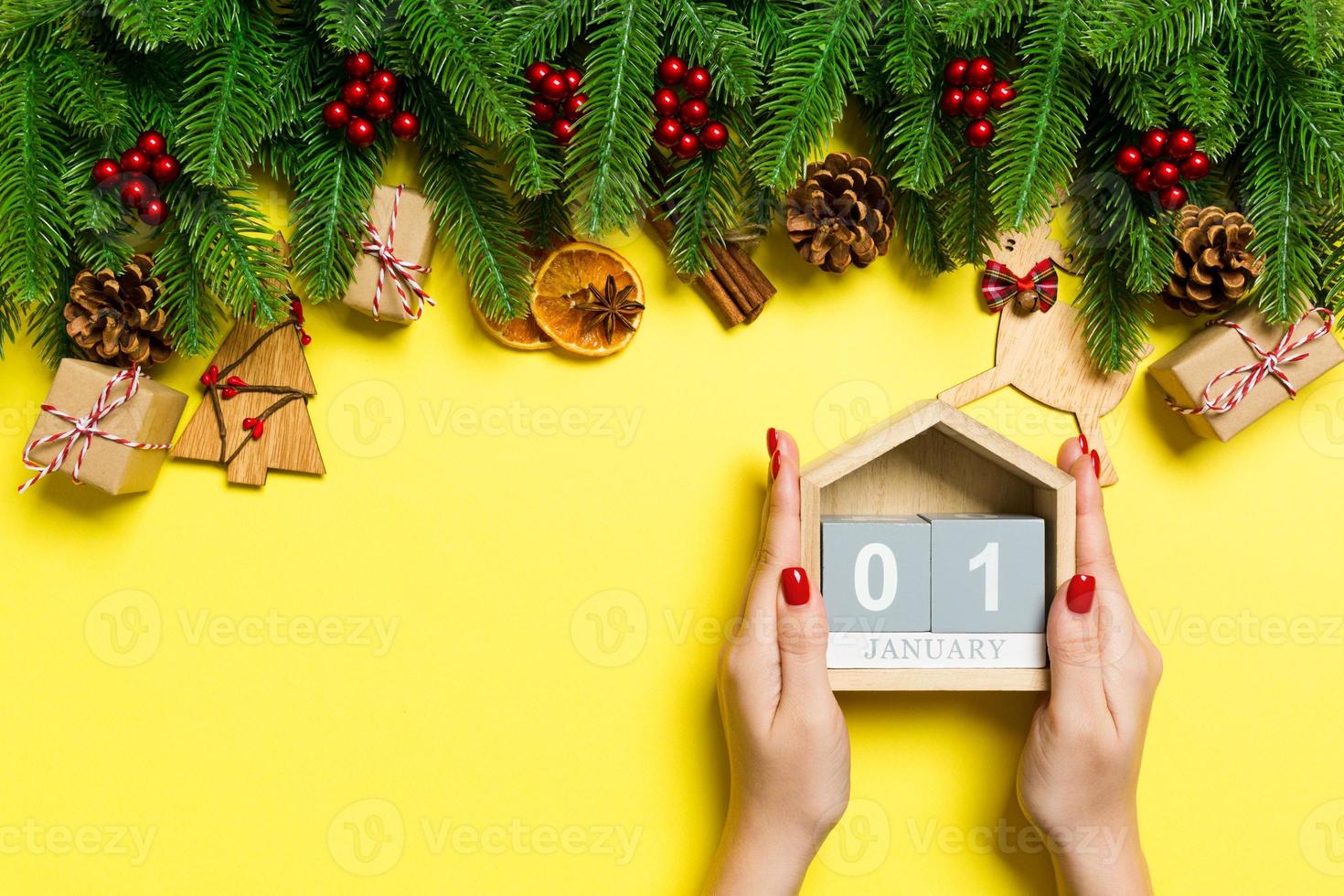 Top view of female hands holding calendar on yellow background. The first of January. Holiday decorations. New Year concept photo