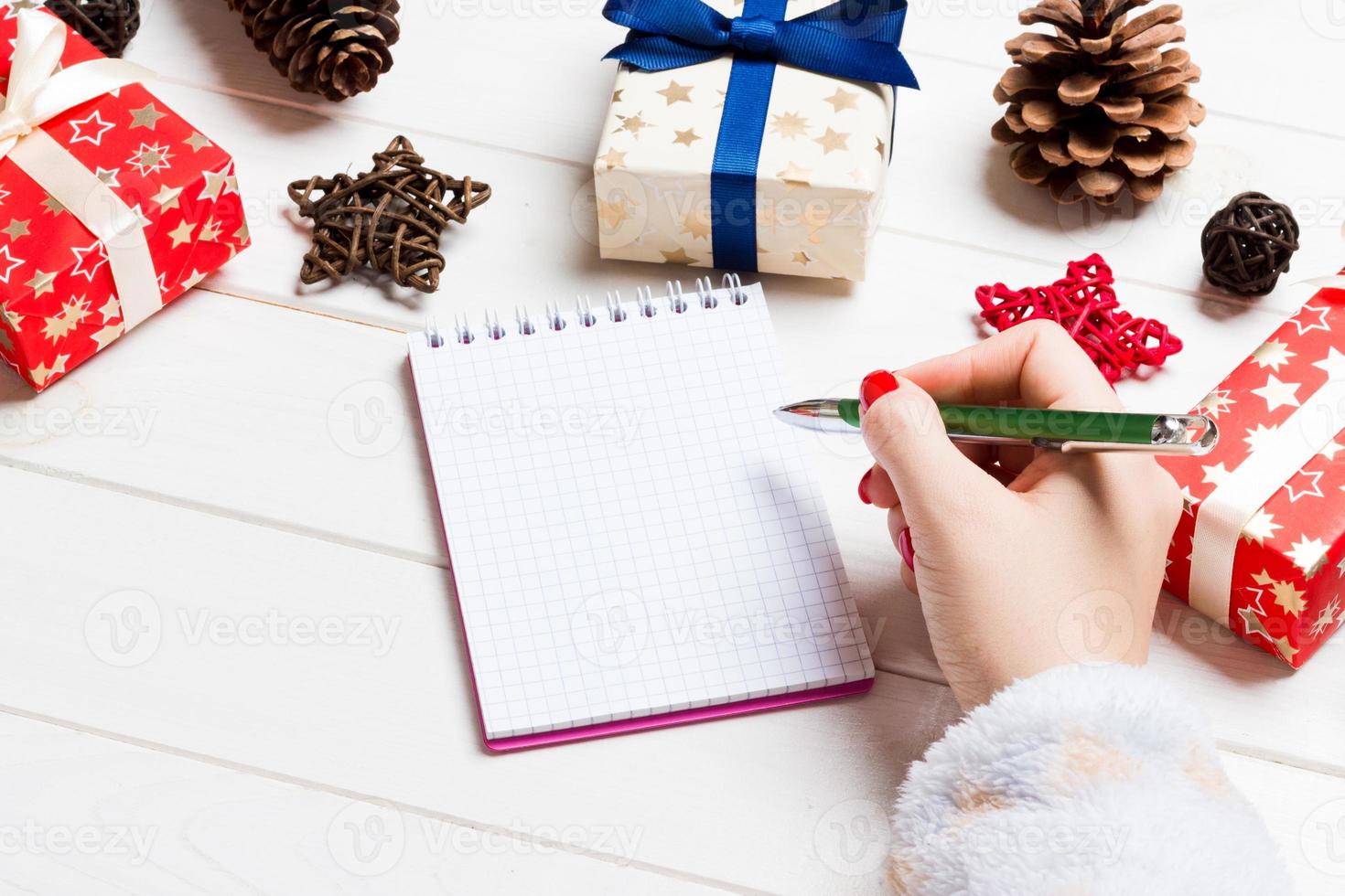 vista superior de la mano femenina escribiendo en un cuaderno sobre fondo de Navidad de madera. lista de deseos concepto de año nuevo foto