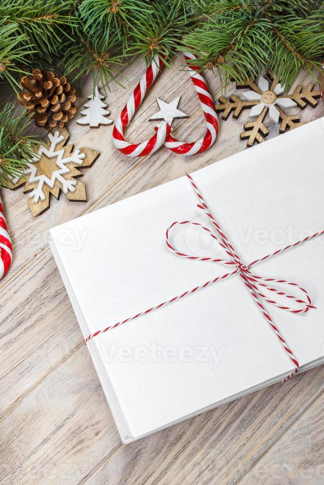 Envelope with blank sheet of paper on Christmas background - fir branch, pine cones, red ribbon, star and heart of sweets. Space for your text photo