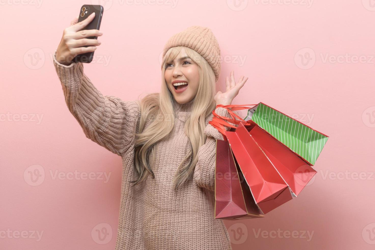 Portrait of Caucasian young woman wearing sweater holding  shopping bag over pink background photo