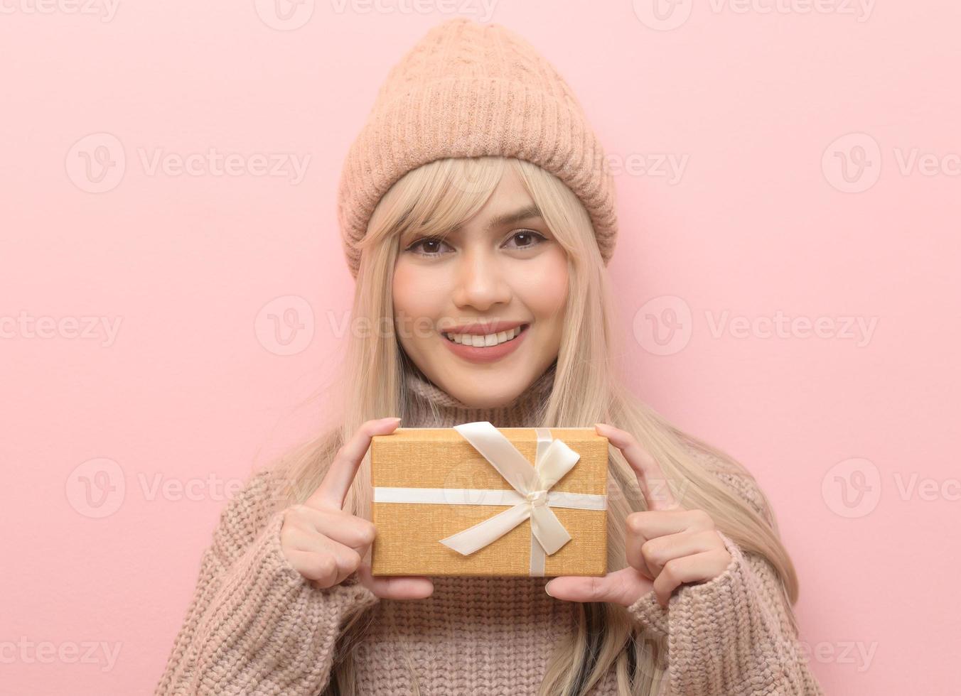 Portrait of Caucasian young woman wearing sweater holding gifts box  over Pink background photo