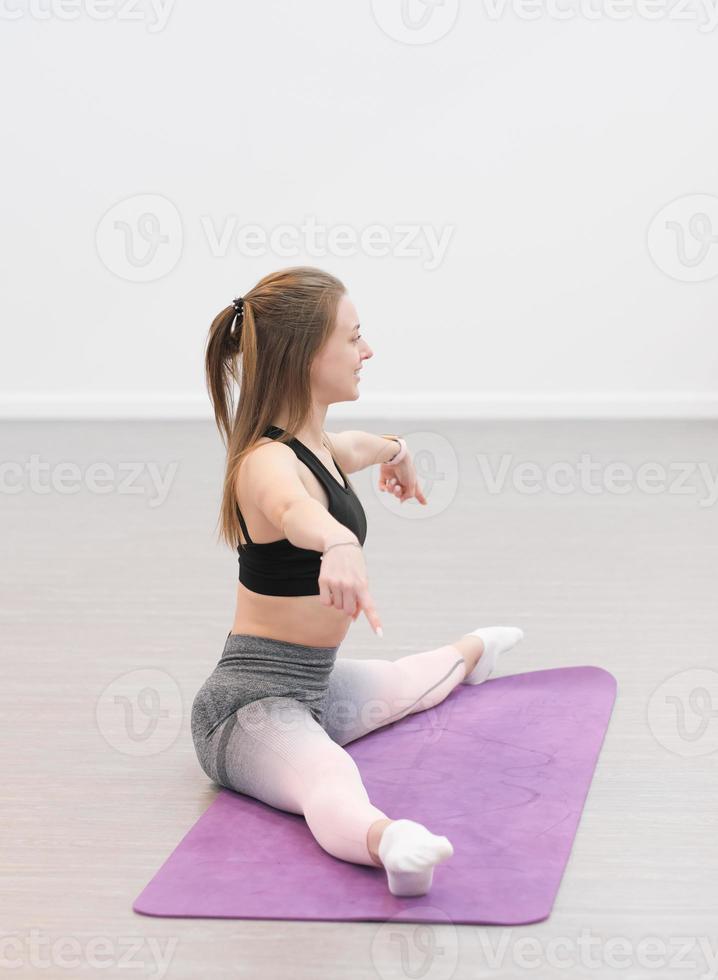 young pretty woman doing pilates and stretching workout on a mat. side view of woman sitting on a floor and stretching leg, split . photo