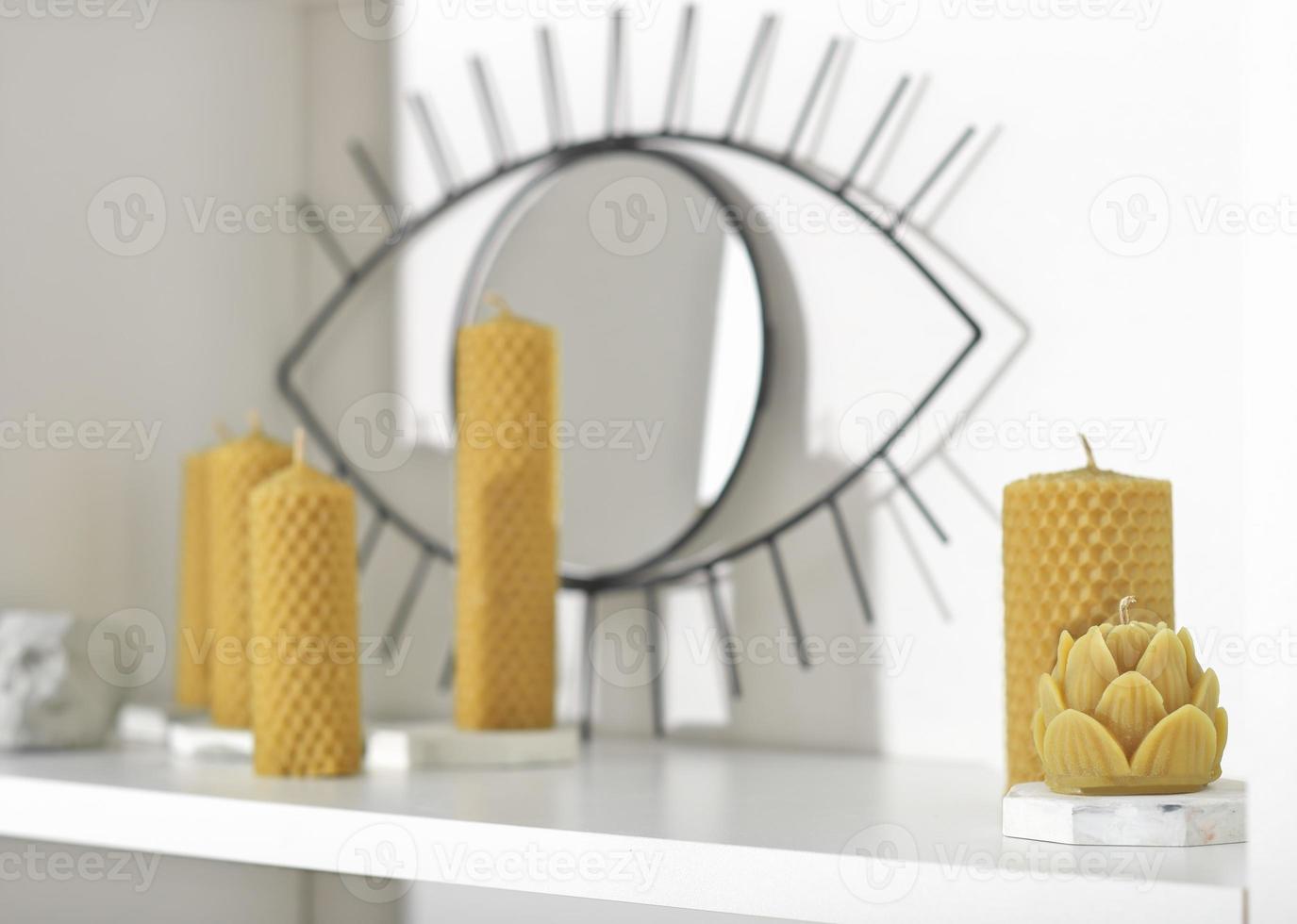 various beeswax candles on white shelf. handmade candles on concrete candlesticks. trendy hipster interior design. natural eco decor for modern room. photo