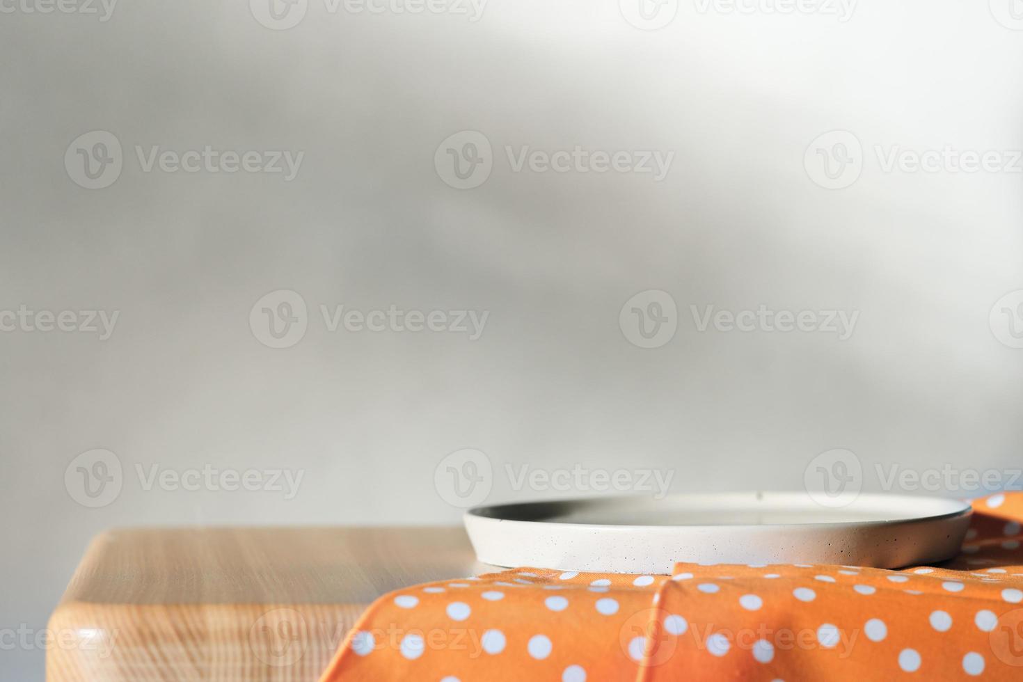 Empty concrete plate on orange tablecloth on wooden table over grunge grey background. side view. copy space for food placement photo