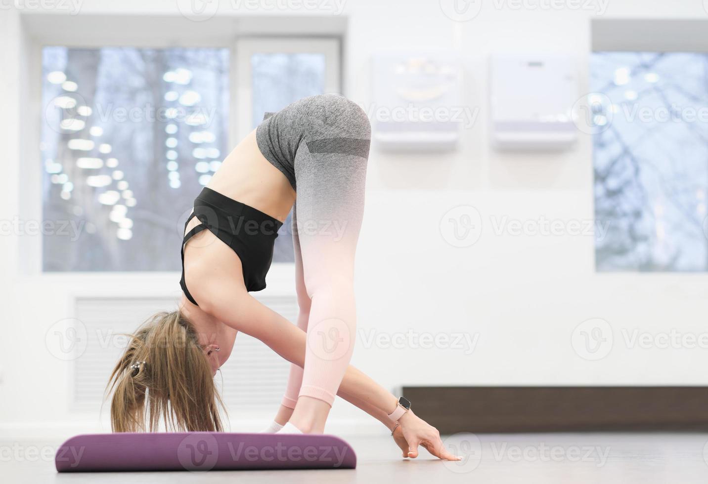 mujer joven deportiva delgada haciendo curvas hacia adelante en el gimnasio. entrenamiento diario, estilo de vida activo y estiramiento de las articulaciones. foto