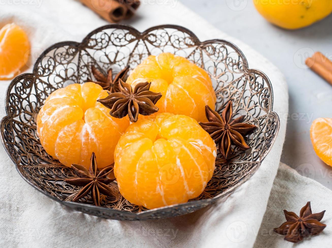 Fresh mandarins in a plate with fir tree branches, star anise cinnamon on gray background photo