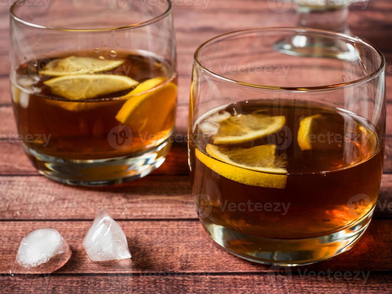 Glasses of cocktail with ice and lemon on wooden table close-up photo