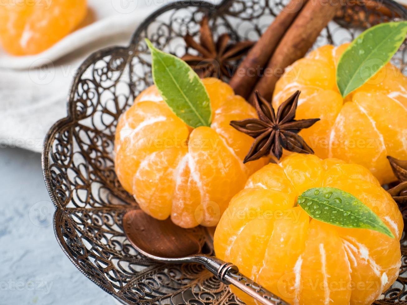 Fresh mandarins in a plate with fir tree branches, star anise cinnamon on gray background photo