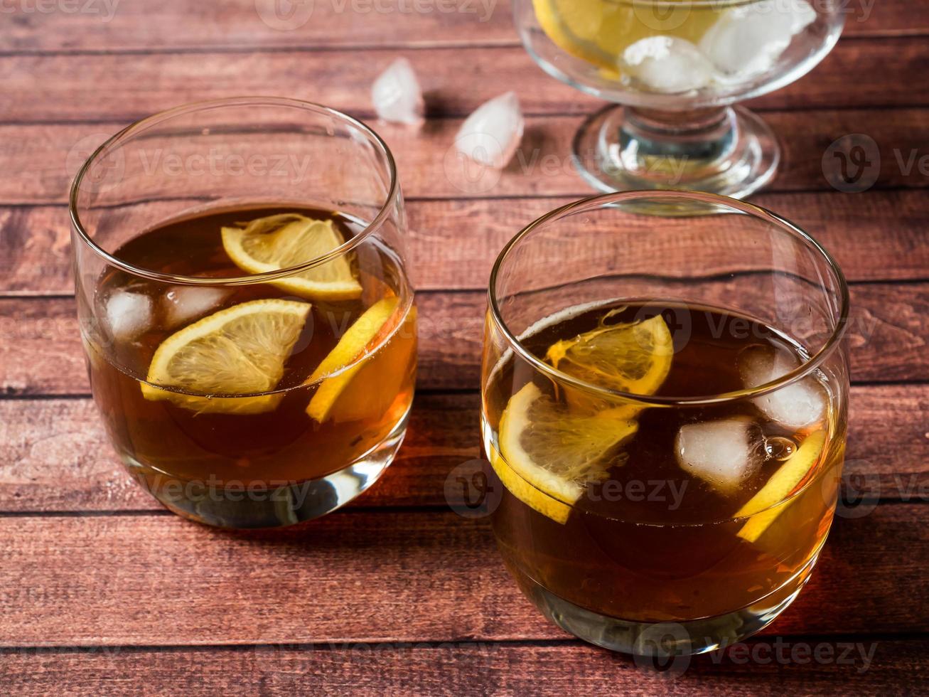 Glasses of cocktail with ice and lemon on wooden table close-up photo