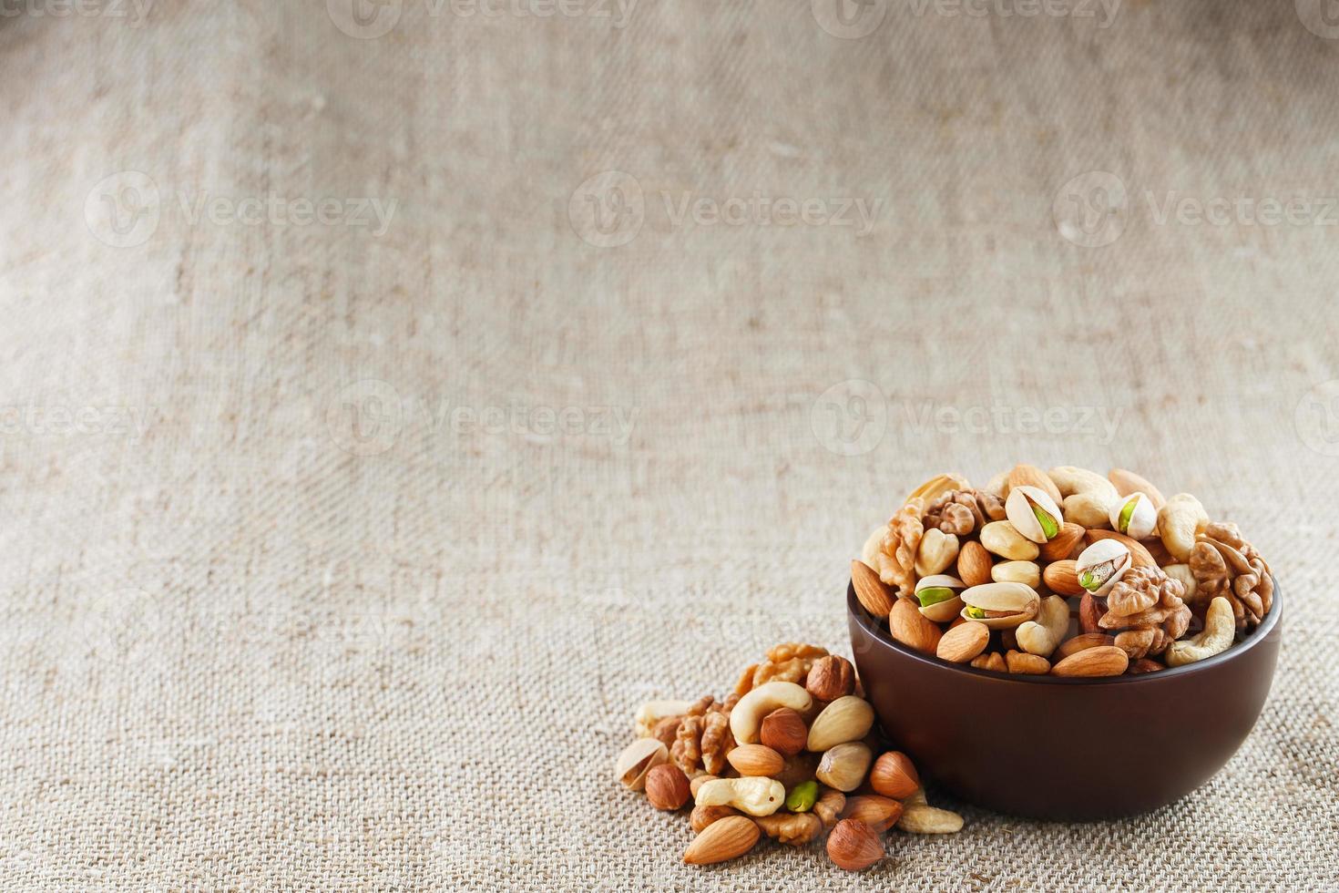 Mix of different nuts in a wooden cup against the background of fabric from burlap. Nuts as structure and background, macro. Top view. photo