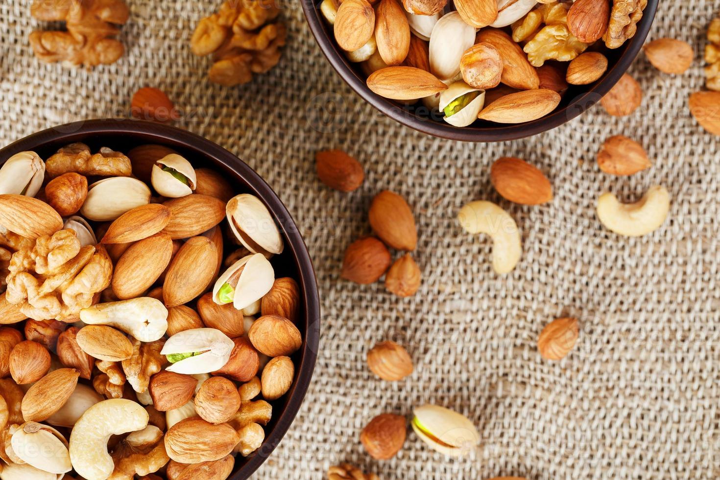 Mix of various nuts in a wooden cup against the background of fabric from burlap. Nuts as structure and background, macro. Top view. photo