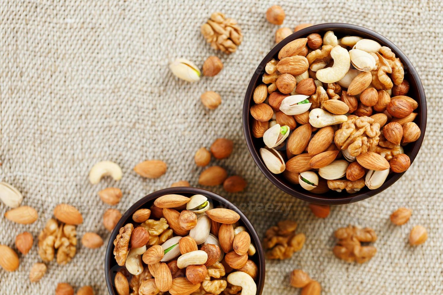 Mix of various nuts in a wooden cup against the background of fabric from burlap. Nuts as structure and background, macro. Top view. photo