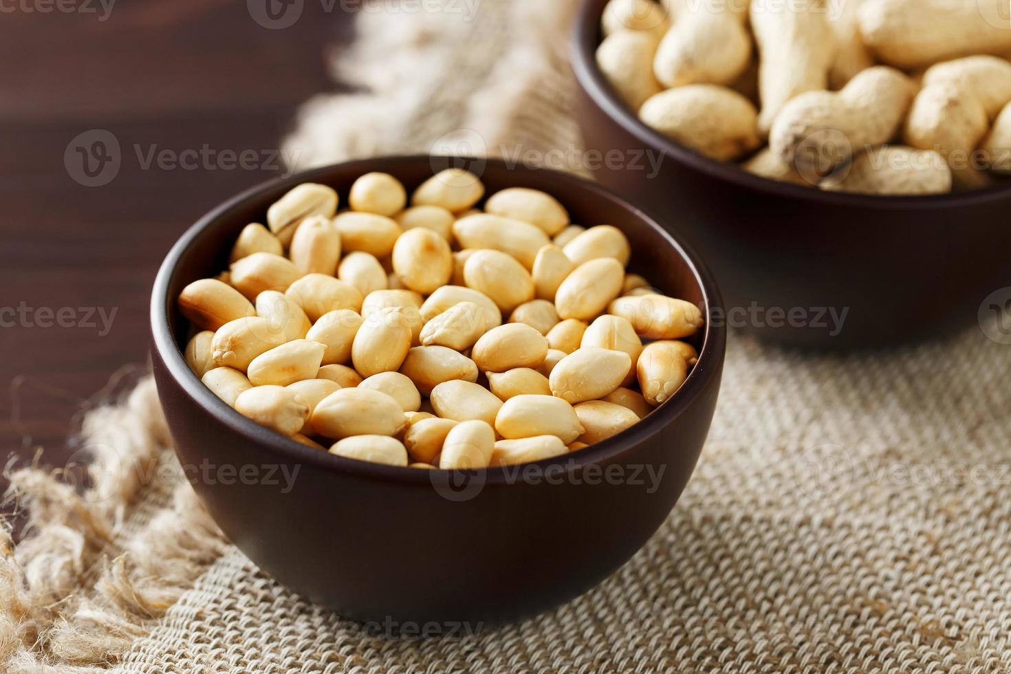 cacahuetes con cáscara y primer plano pelado en tazas. cacahuetes tostados con cáscara y pelados contra un paño marrón. foto