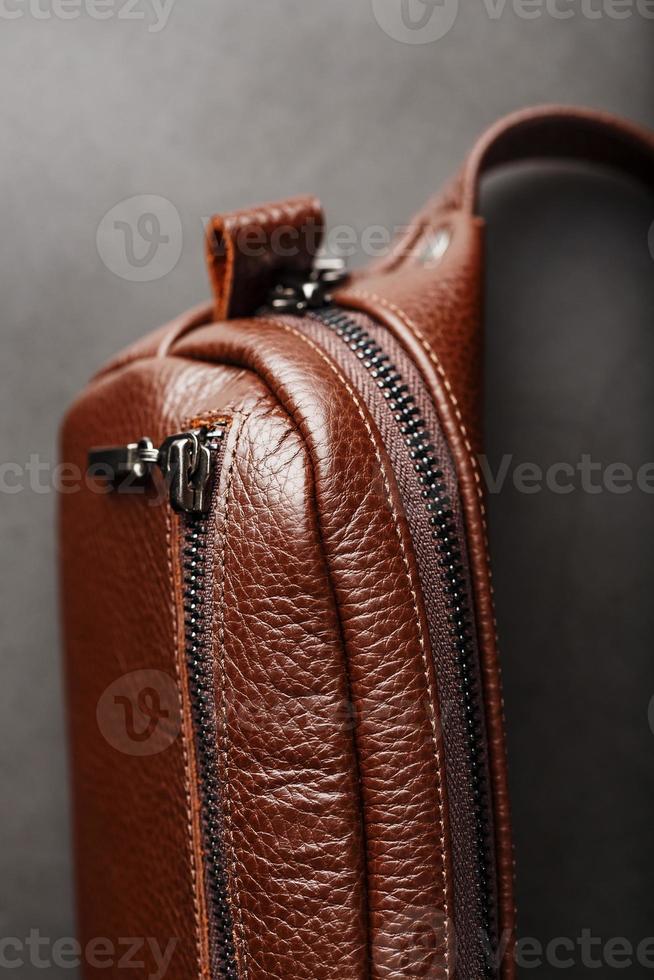 A brown belt bag made of textured brown leather on a black stone background. Elegant fanny pack brown bag with a zipper photo