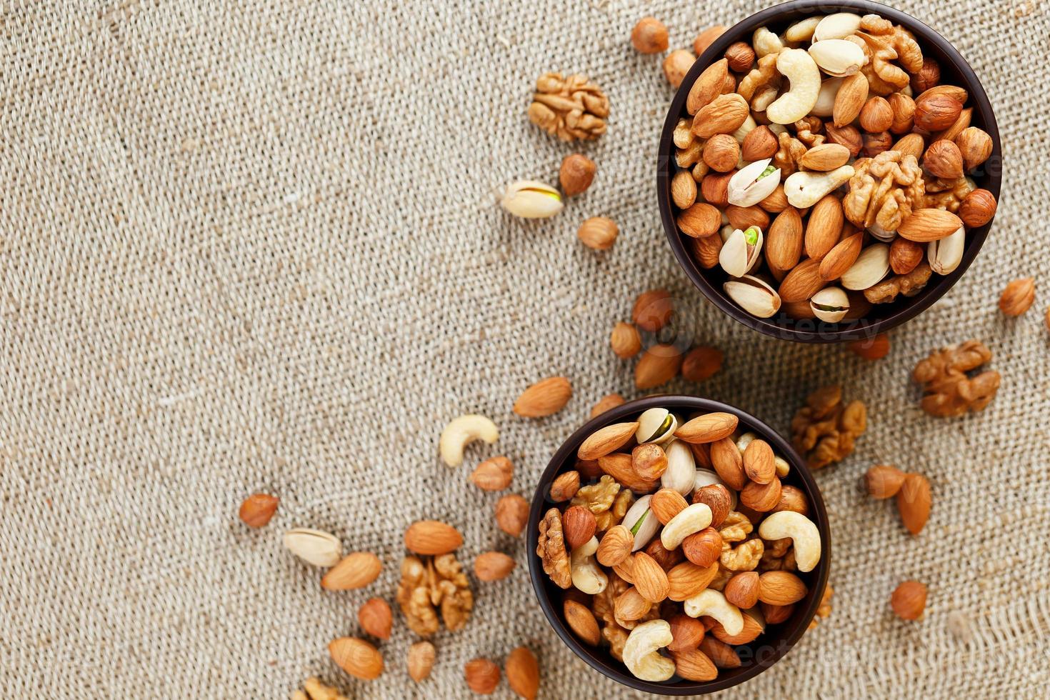 Mix of various nuts in a wooden cup against the background of fabric from burlap. Nuts as structure and background, macro. Top view. photo