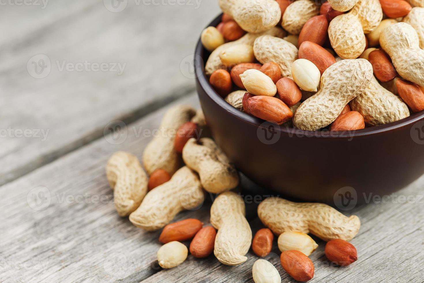 Roasted peanuts in the shell and peeled in a cup, against a gray wooden