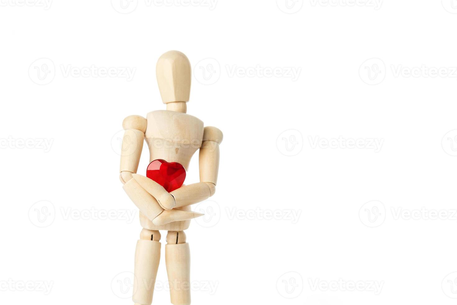 The wooden figure of a man holds in his hands a red heart on a white background. Gives the heart photo