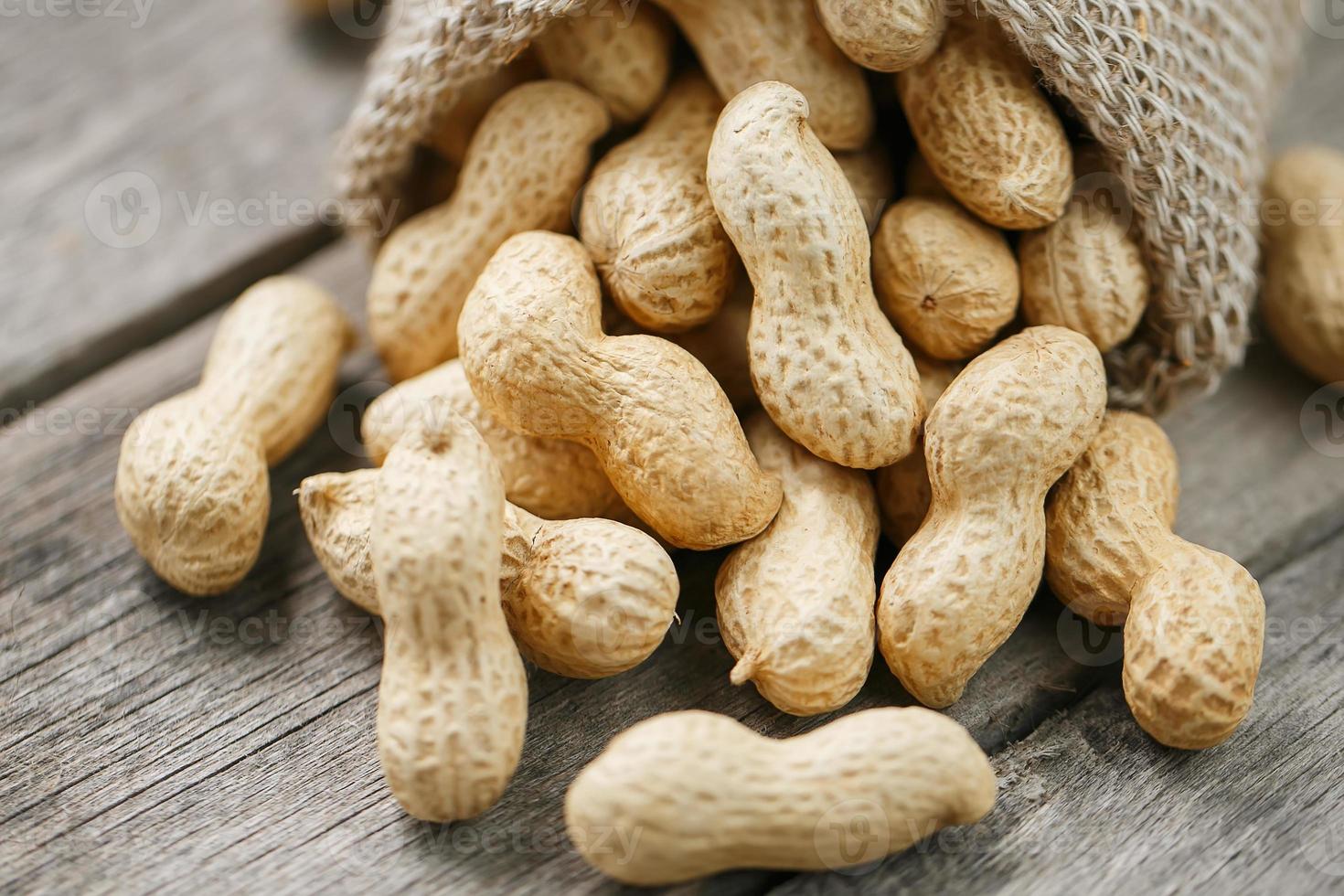 Peanuts in a miniature burlap bag on old, gray wooden surface photo