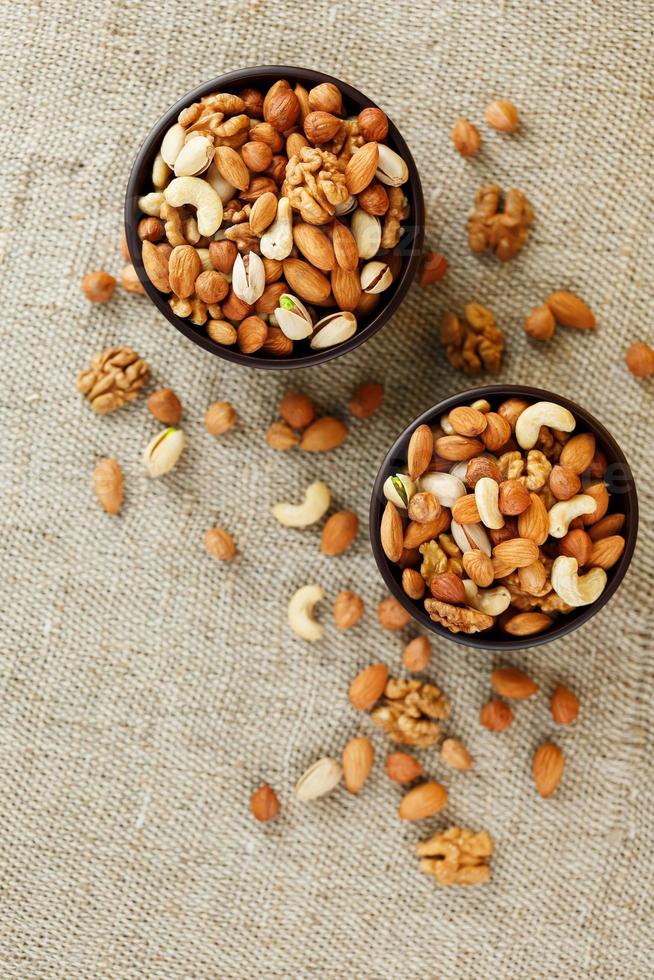 Mix of various nuts in a wooden cup against the background of fabric from burlap. Nuts as structure and background, macro. Top view. photo