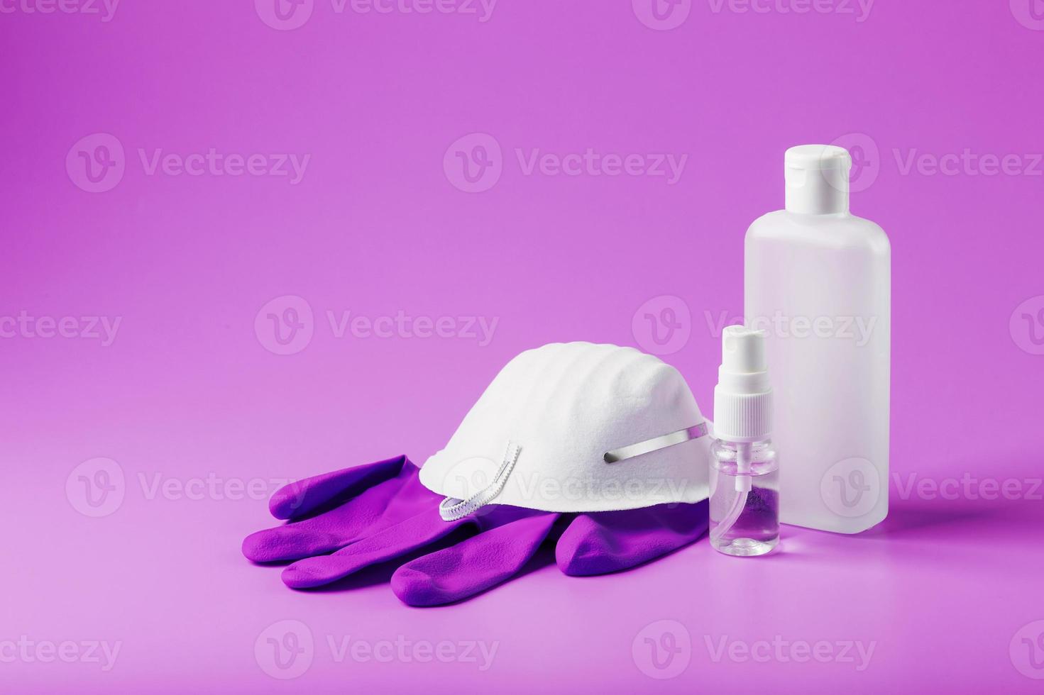 Bodegón de protección antivirus sobre fondo rosa, máscara, guantes de goma, una botella de desinfectante para manos, gel antiséptico. foto